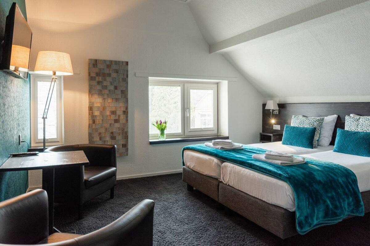 A hotel room with a bed, a desk, a chair, and a window with a view of greenery.