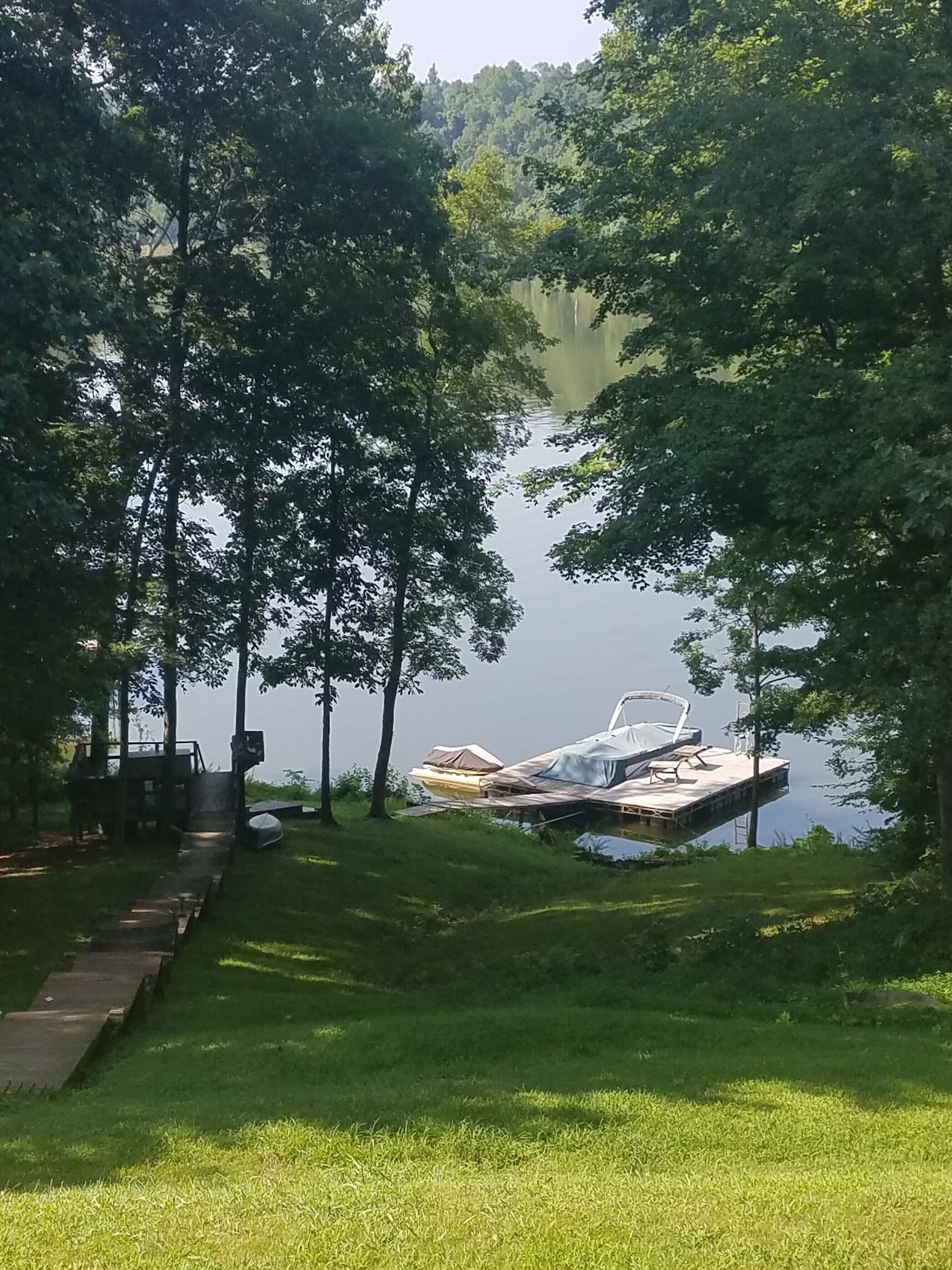 Une jetée qui s’avance dans un lac, entourée d’arbres et d’une zone herbeuse.