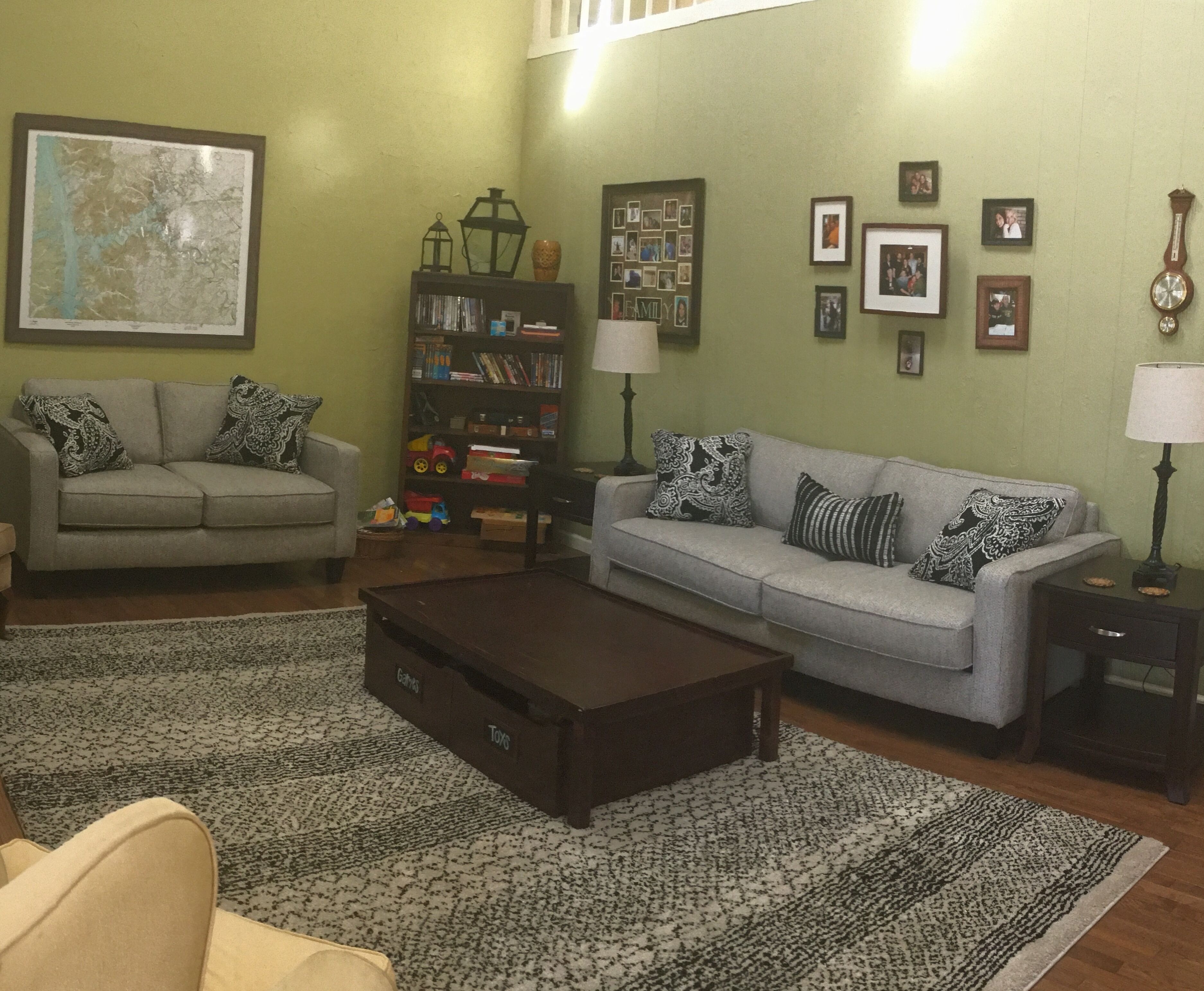 A living room with a sofa, armchairs, a coffee table, a bookshelf, and a map on the wall.