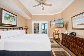 Une chambre d’hôtel avec un grand lit, un ventilateur de plafond, un bureau avec un téléphone et une vue sur l’océan depuis la porte.