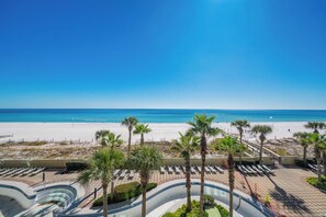 Vista a la playa con palmeras, una zona de piscina y un cielo azul despejado.