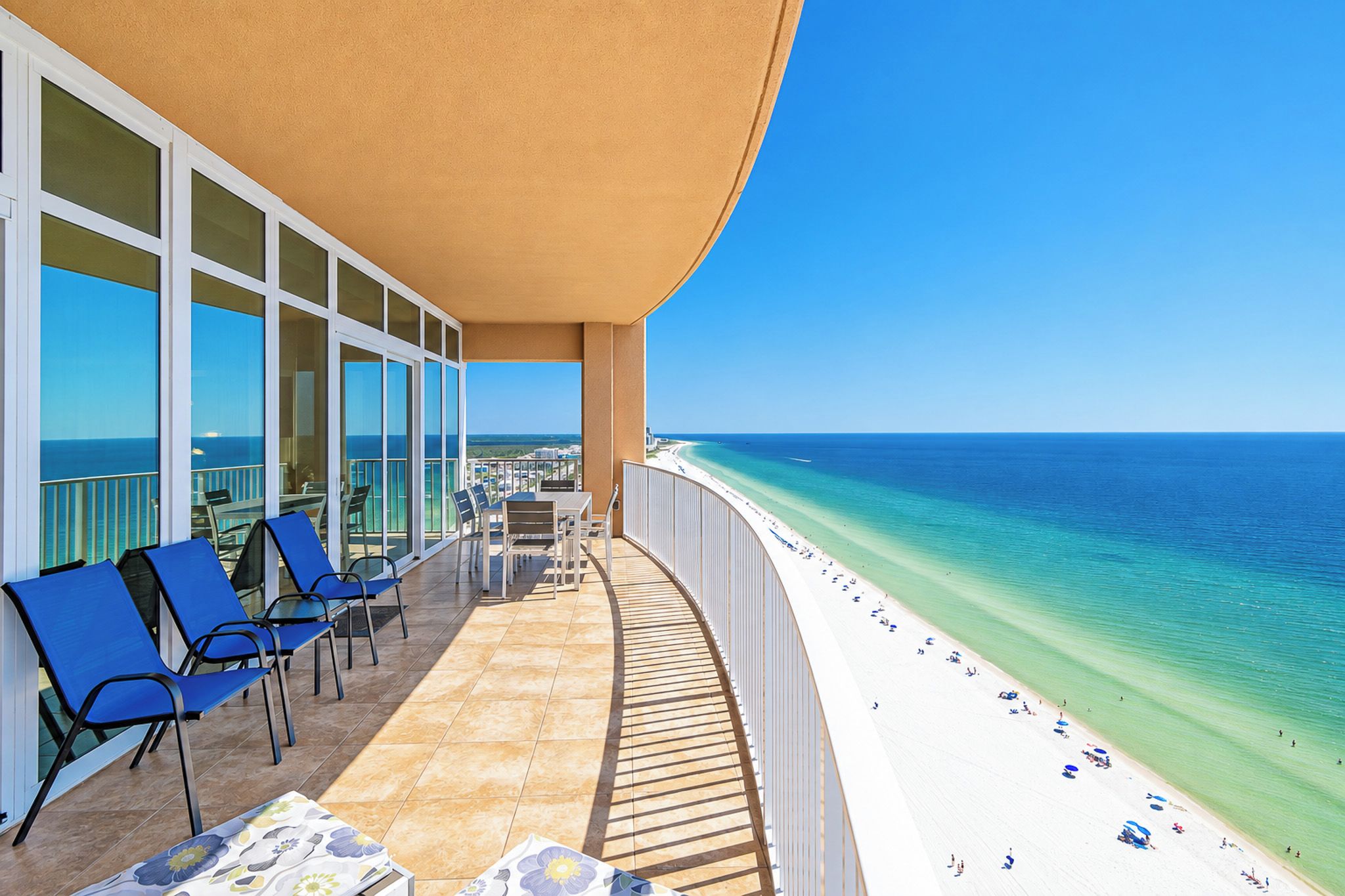 Un balcon avec des chaises bleues et une table, donnant sur une plage aux eaux turquoise et cristallines.