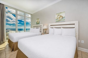 Ein Hotelzimmer mit zwei Betten, einem großen Fenster mit Blick auf den Strand und Bildern an den Wänden.