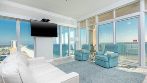 A spacious balcony with a white sofa, two patterned armchairs, and a flat-screen TV.