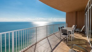 A balcony with a view of the ocean, a table with chairs, and a glass door.