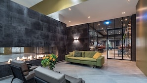 A modern lobby with a fireplace, seating area, and a glass partition leading to a dining area. - Van der Valk Hotel Leeuwarden (Leeuwarden)