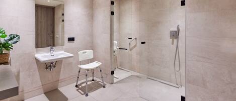 Un baño moderno con ducha envuelta en vidrio, un lavamanos blanco y una silla.