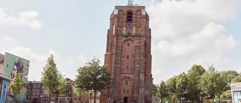 A historic brick tower with a clock, surrounded by a paved square with trees and buildings.