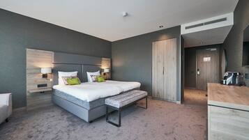 Een moderne hotelkamer met een groot bed, bedlampen, een bankje, een houten hoofdbord en een klein bureau met een spiegel.