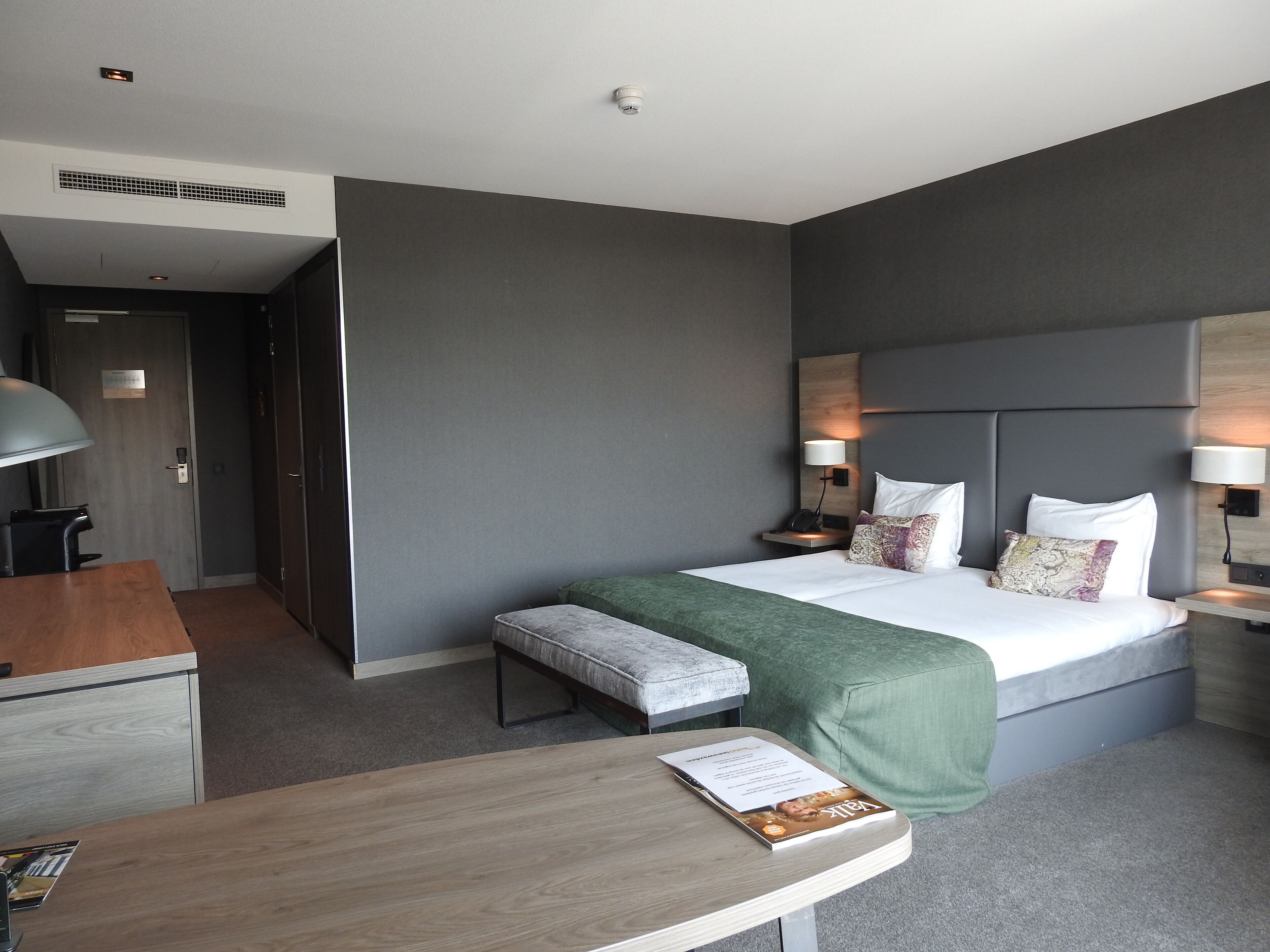 Una habitación de hotel moderna con una cama grande, mesitas de noche con lámparas, un escritorio y una silla.