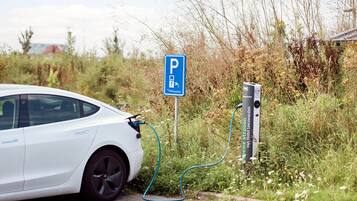 A white car parked next to a charging station with a blue parking sign.