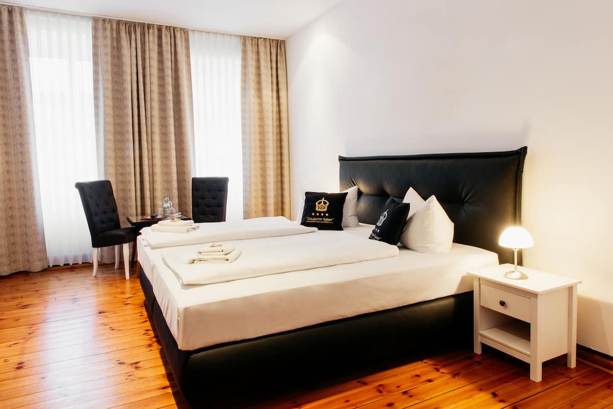 A hotel room with a large bed, a bedside table with a lamp, a chair, and a desk.