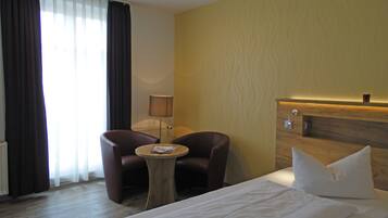 A hotel room with a bed, two armchairs, a small round table, a lamp, and a wooden headboard.