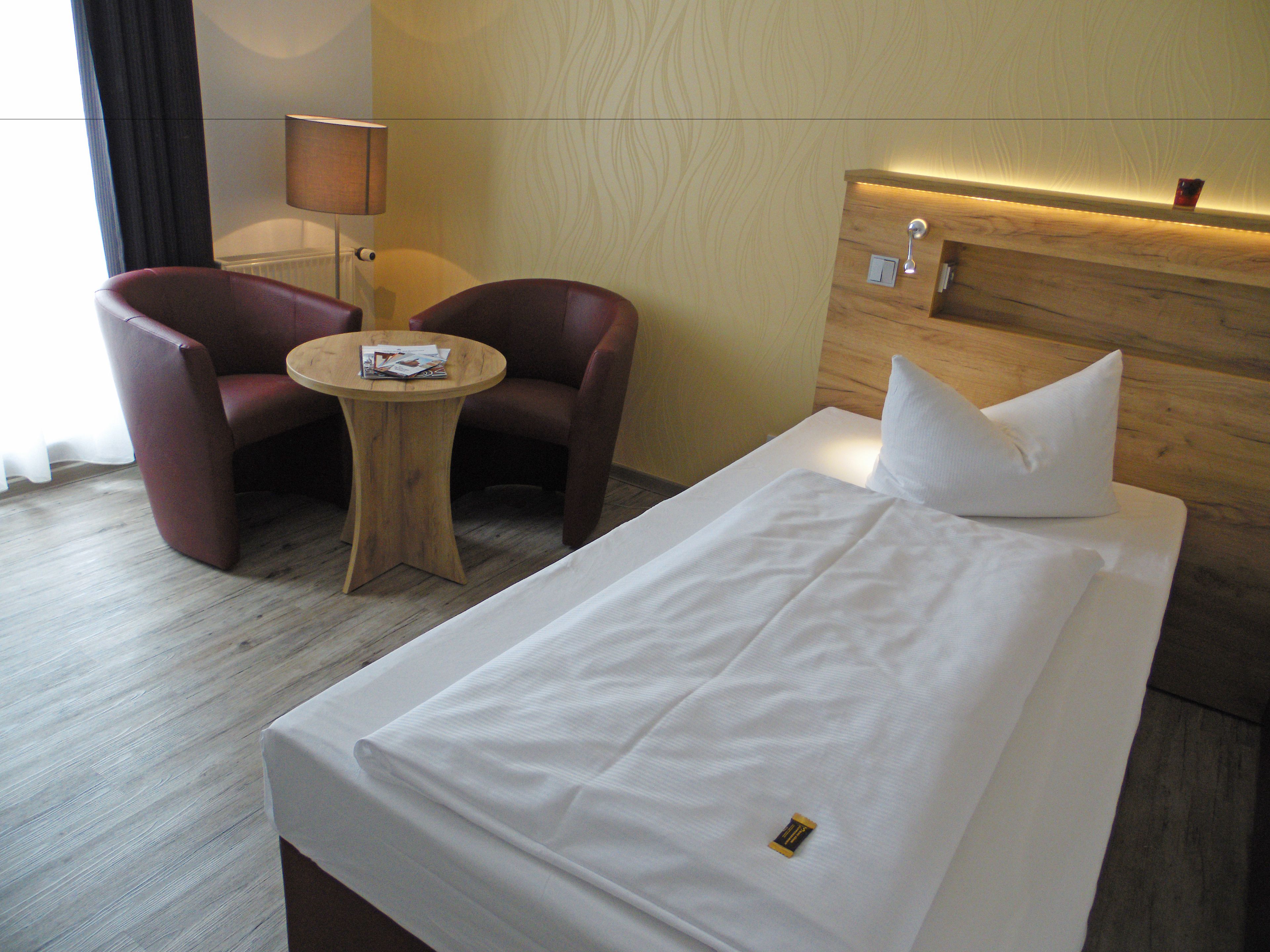 Habitación de hotel con una cama individual, dos sillones, una mesita de madera y una lámpara.