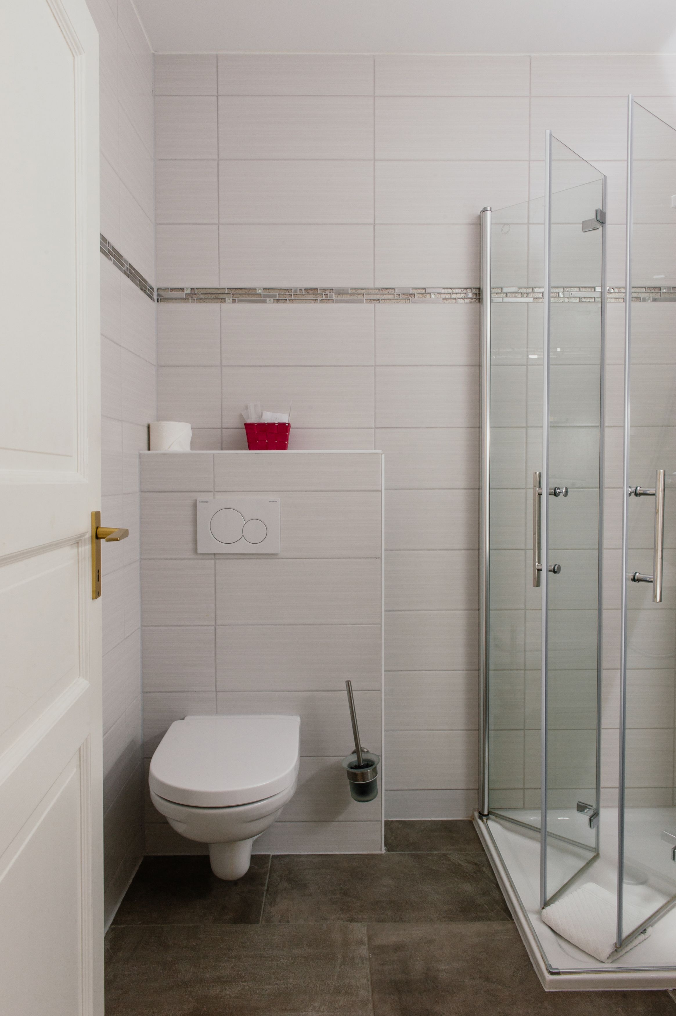 A compact bathroom with a toilet, a shower enclosure, and a red basket on the wall.