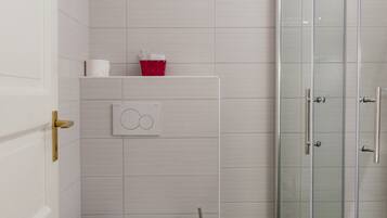 A compact bathroom with a toilet, a shower enclosure, and a red basket on the wall.