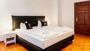 A double bed with black headboard and white bedding, a nightstand with a lamp, and a wooden door.