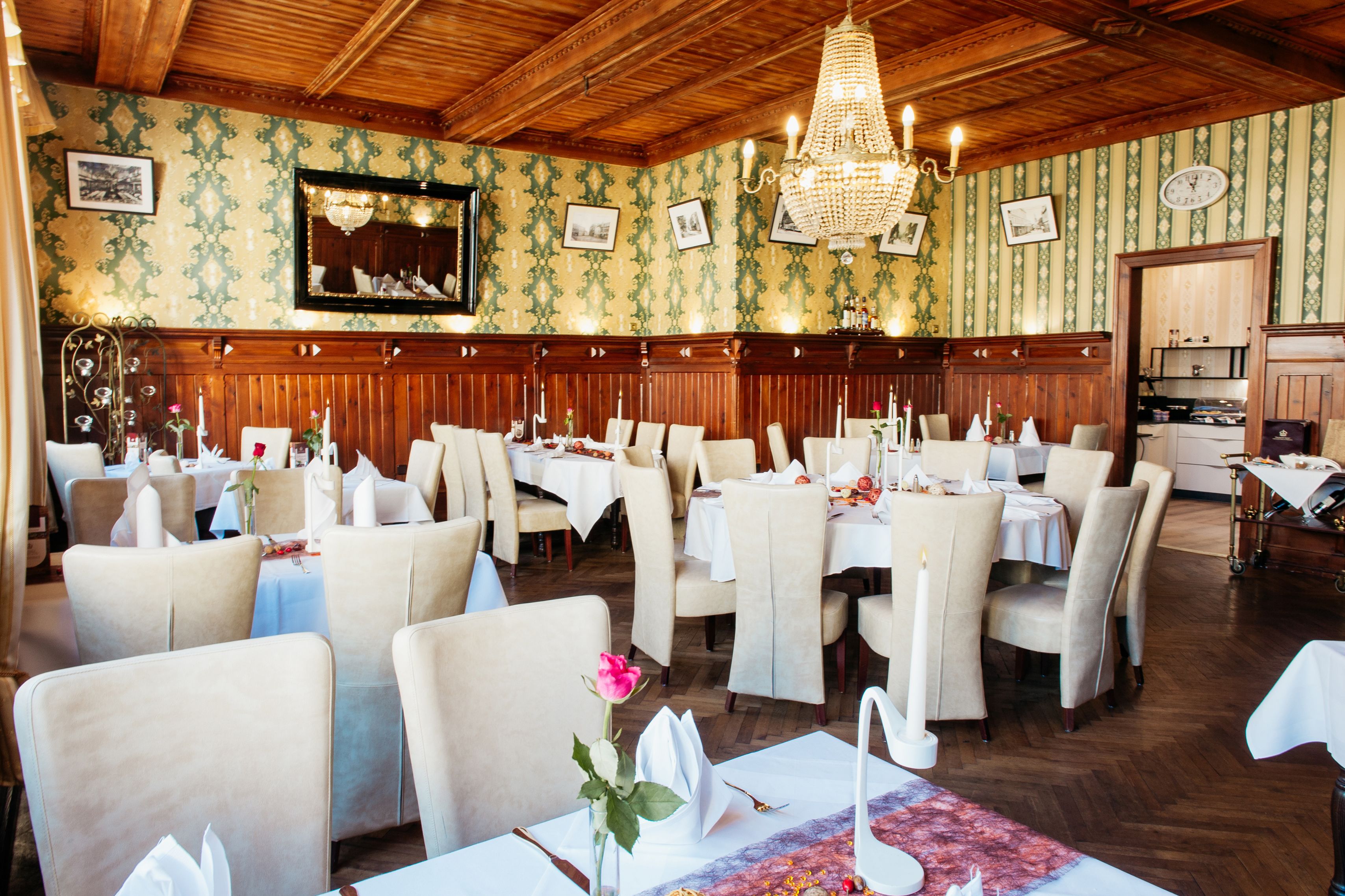 A restaurant with wooden paneling, chandeliers, and a patterned wallpaper interior.