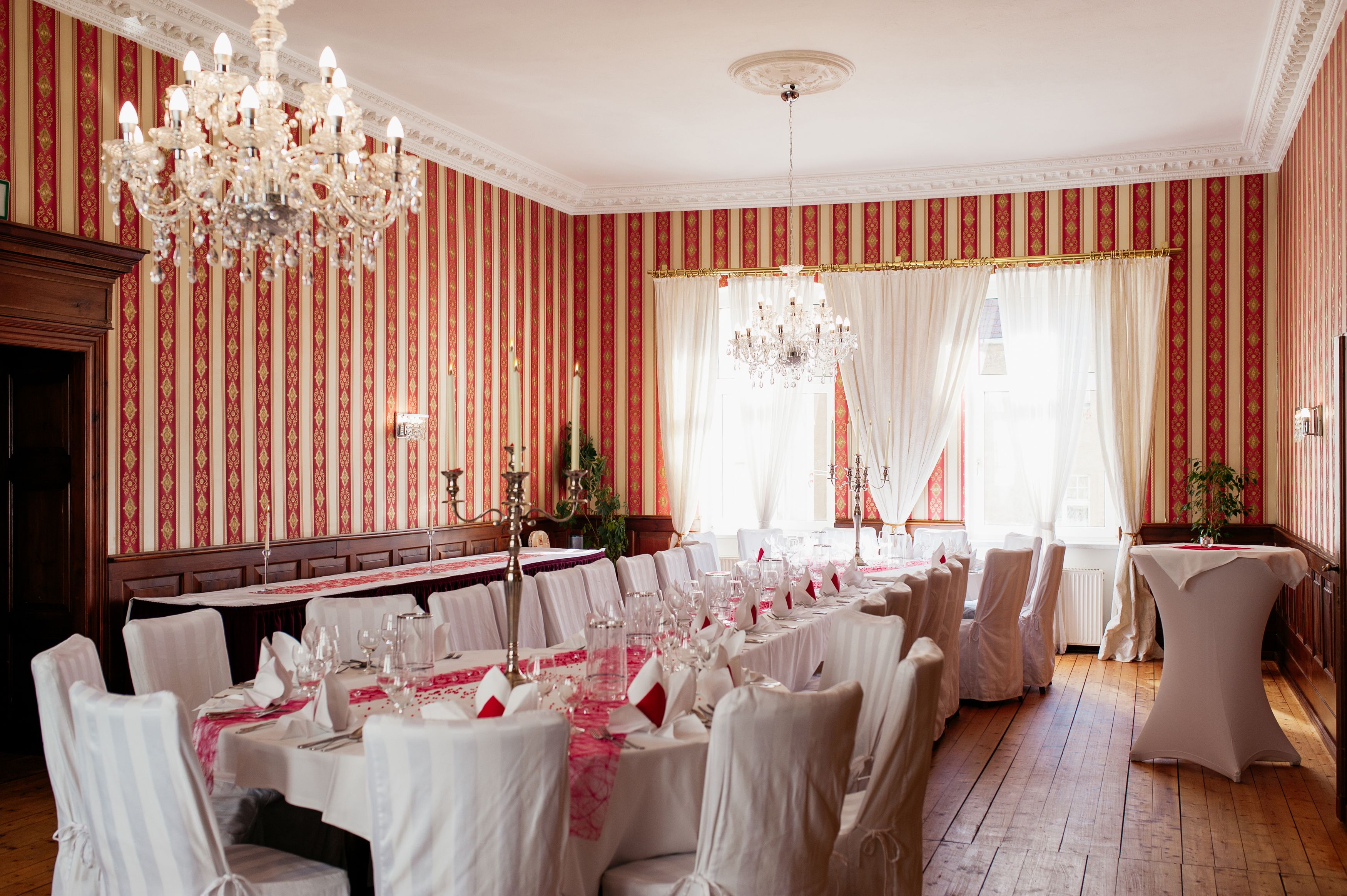 A banquet hall with striped wallpaper, chandeliers, and white table settings.