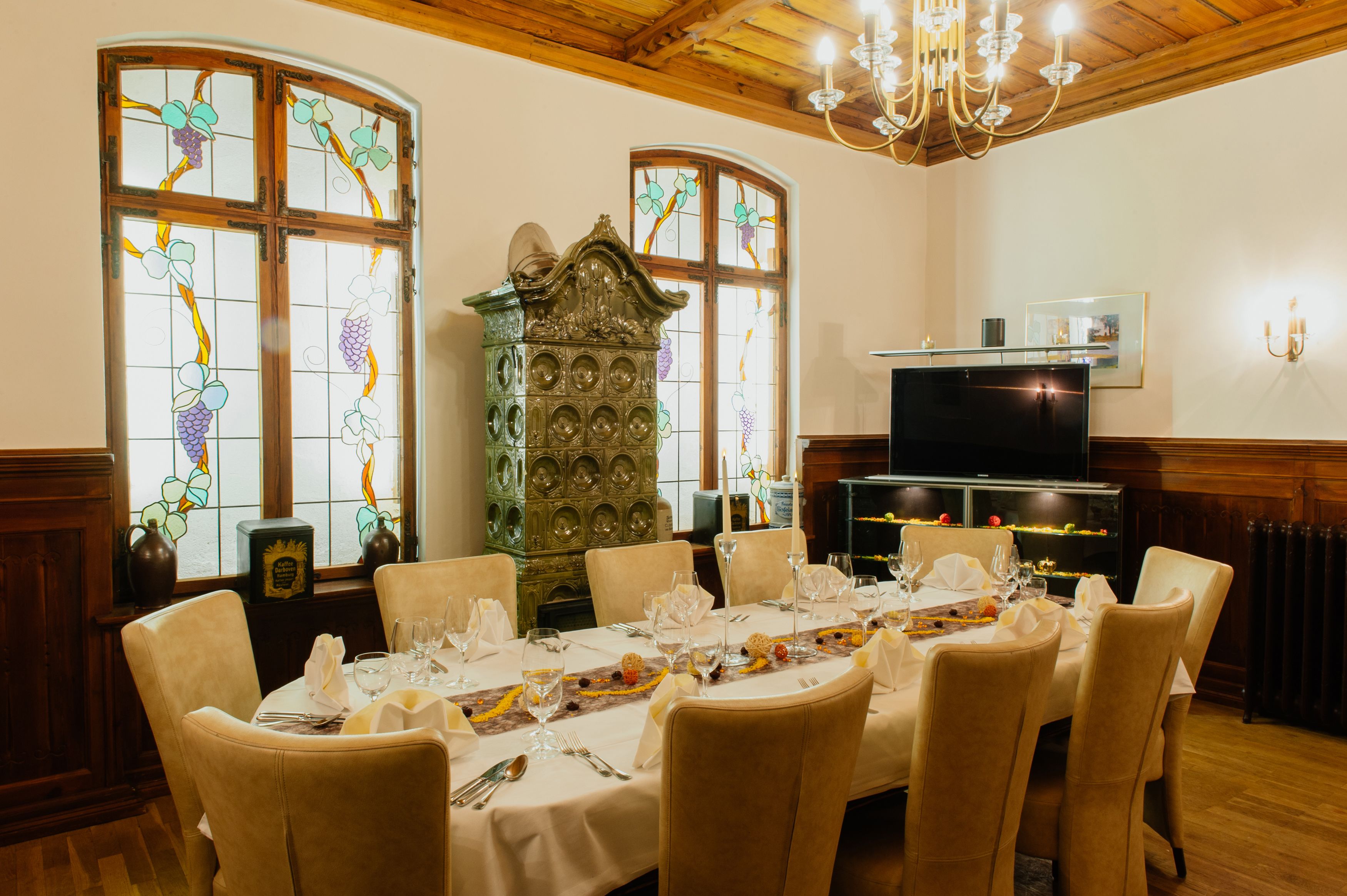 Comedor con una mesa redonda dispuesta para seis personas, rodeada de sillas, con una araña y vidrieras al fondo.