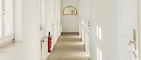 A long, narrow hallway with white walls and wooden flooring, leading to a door at the end.
