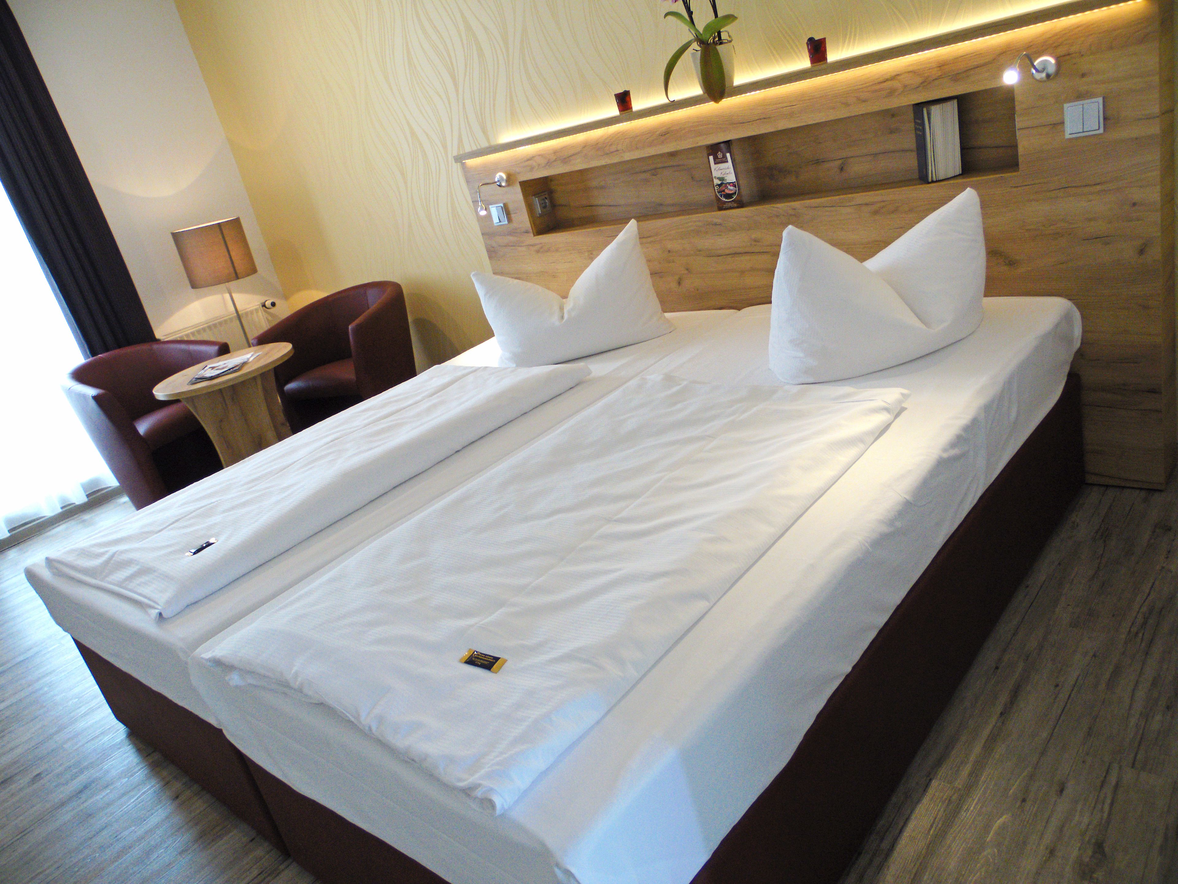 A hotel room with a large bed, a small desk, a chair, and a wooden headboard.