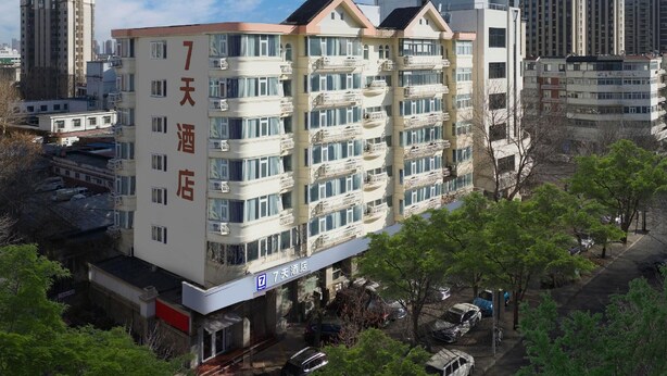 A multi-story hotel with balconies, a clear sky, and surrounding high-rise buildings. - 7 Days Inn (Tianjin)