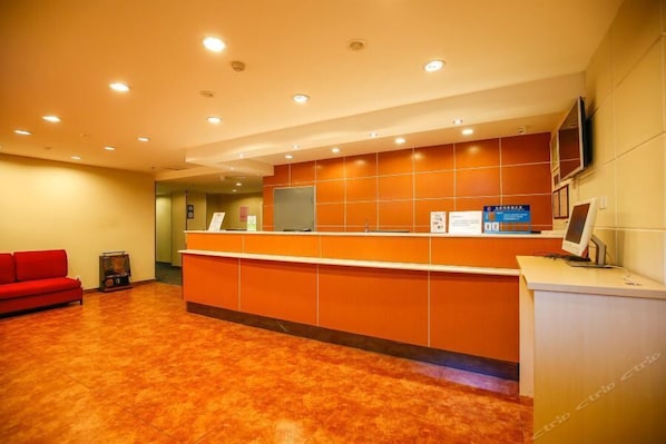 A reception area with a red sofa, a reception desk, and a television screen.