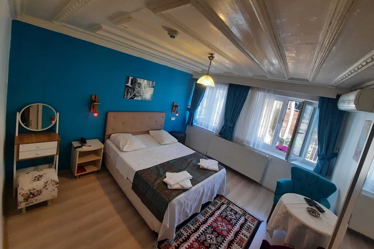 A bedroom with a bed, bedside tables, a mirror, a window with curtains, and a small table with a lamp.