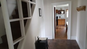 Un couloir avec un escalier, un coin cuisine à l’arrière-plan et une décoration murale en bois.