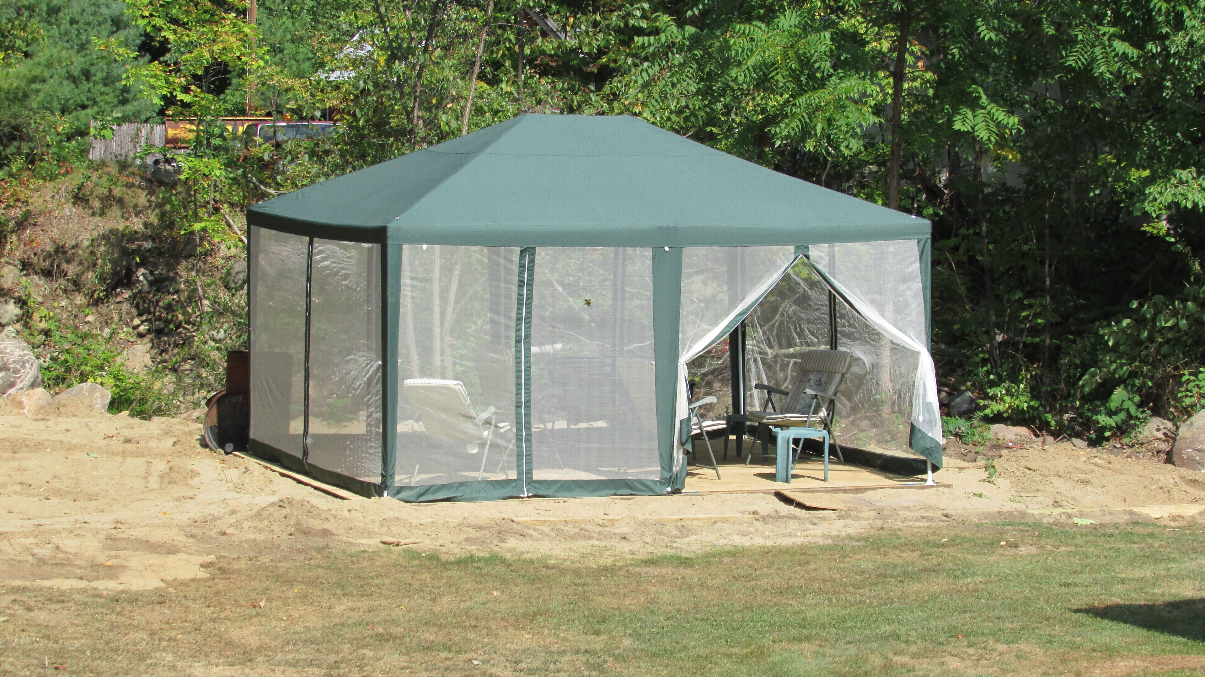 Uma tenda verde com tela lateral e toldo, montada em área gramada com árvores ao fundo.