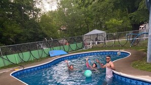 Une piscine à bord incurvé, entourée d’une clôture en treillis métallique et d’arbres.