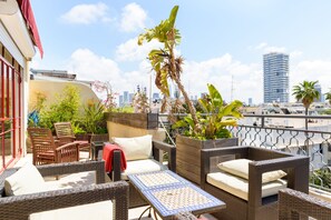 A balcony with wicker furniture, a table, and potted plants. - Amazing Duplex Penthouse with 2 Terraces by FeelHome (Tel Aviv)