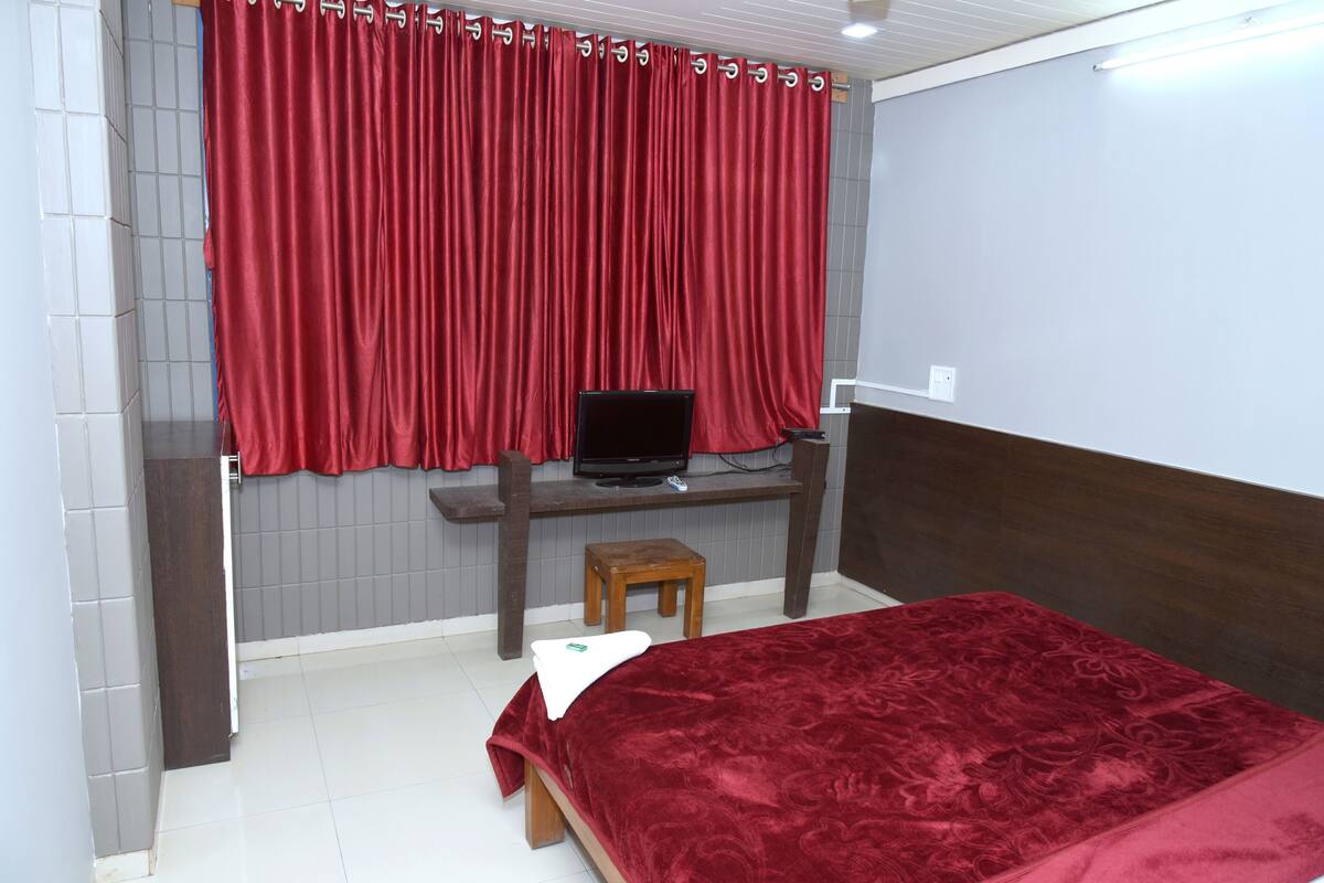Un dormitorio con una cama, un escritorio con computadora y una ventana con cortinas rojas.