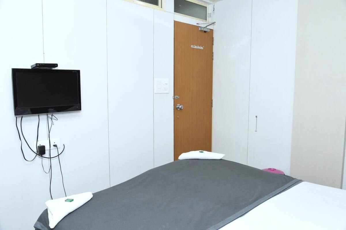 Una habitación con una cama, un televisor montado en la pared y una puerta con un panel de madera.