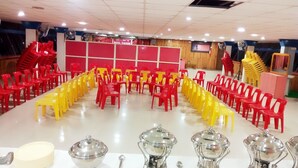 Un salón de conferencias con filas de sillas rojas y amarillas dispuestas para una reunión.