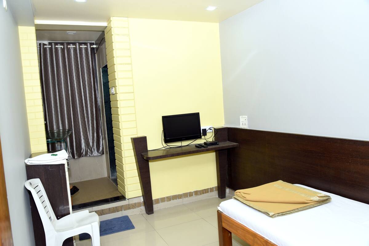 Habitación de hotel con cama, escritorio con computadora, una silla y baño visible tras una cortina.