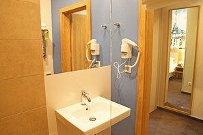 A bathroom with a sink, two hair dryers mounted on the wall, and a mirror reflecting a room with a bed and a window. - Europa (Kaliningrad)