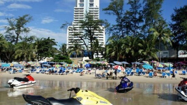 A beach with jet skis, a tall building in the background, and palm trees.