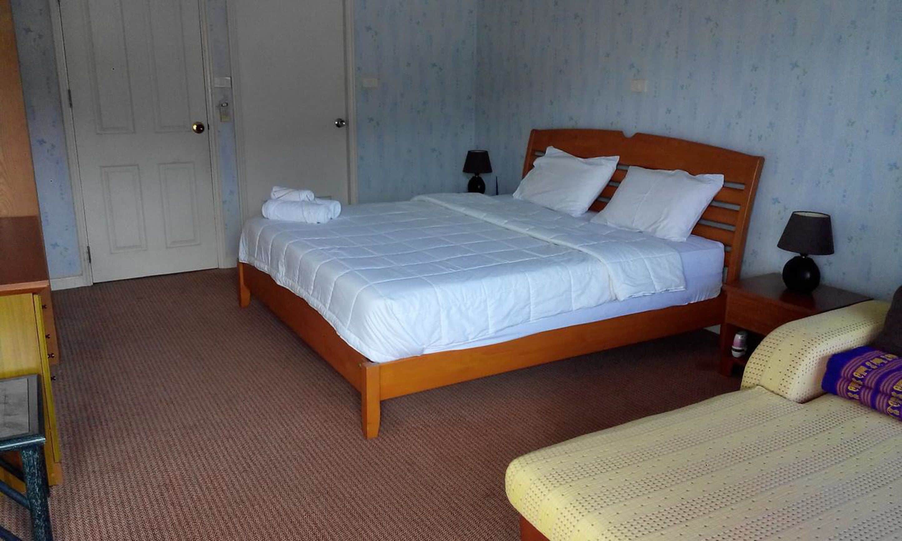 A bedroom with a wooden bed, white bedding, two bedside lamps, a door, and a small table with a lamp.