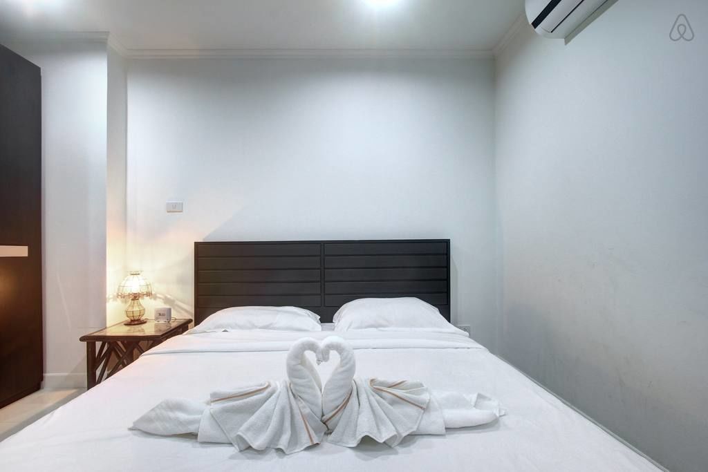 Quarto de hotel com uma cama bem arrumada, uma mesa de cabeceira com abajur e um ar condicionado fixado na parede.