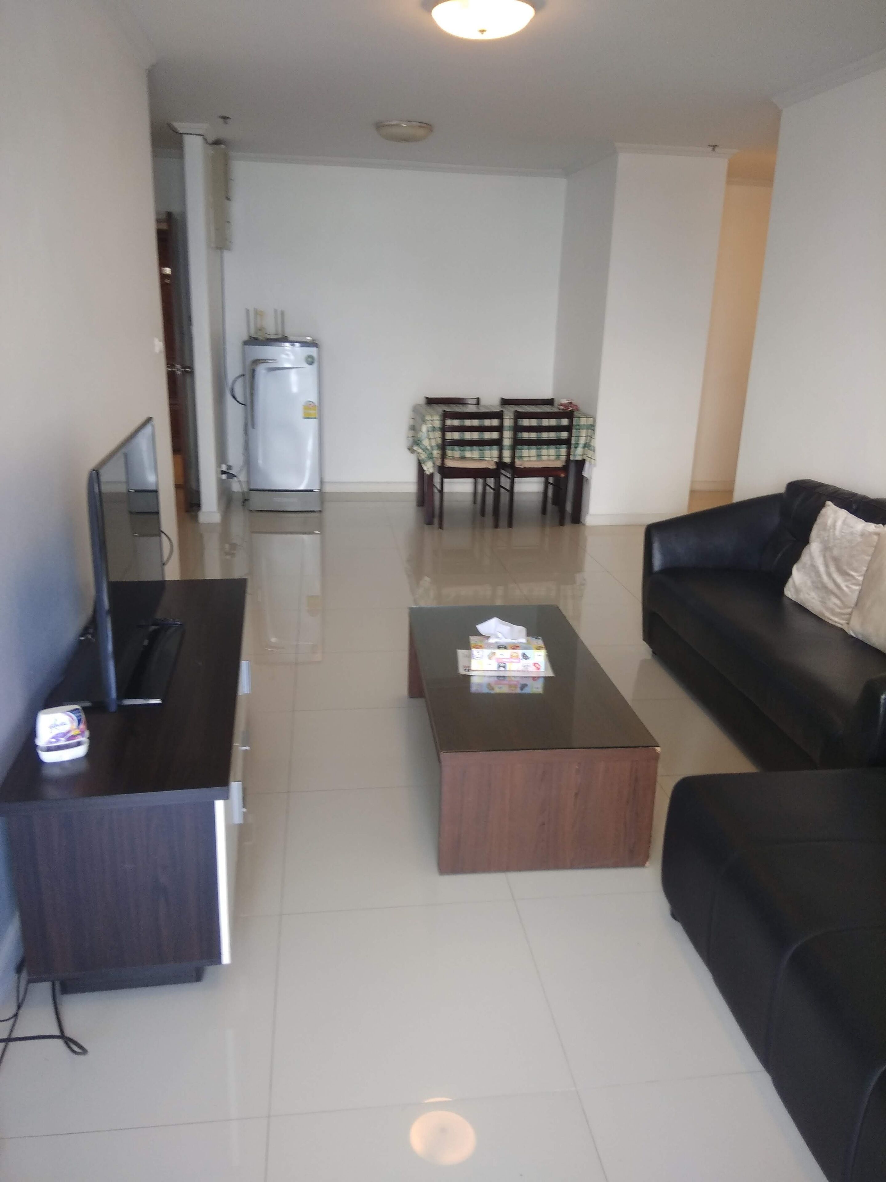 A living room with a black sofa, a wooden coffee table, a TV stand, and a dining area with a table and chairs.