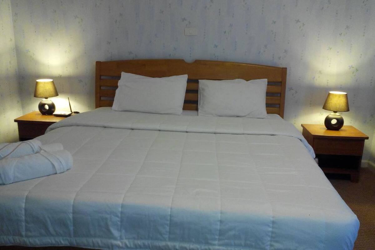 A neatly made bed with white bedding, two bedside lamps, and a folded towel on the left side.