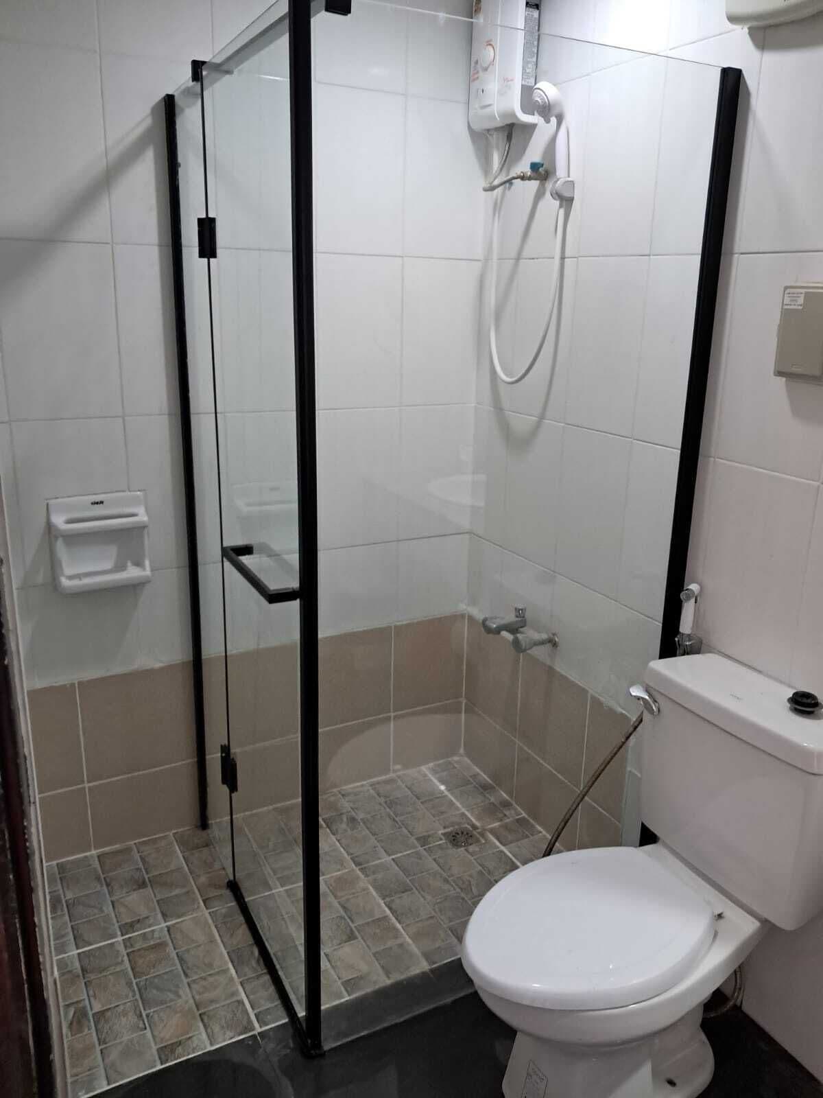 Une salle de bain avec une douche à parois de verre, des toilettes et une petite étagère.