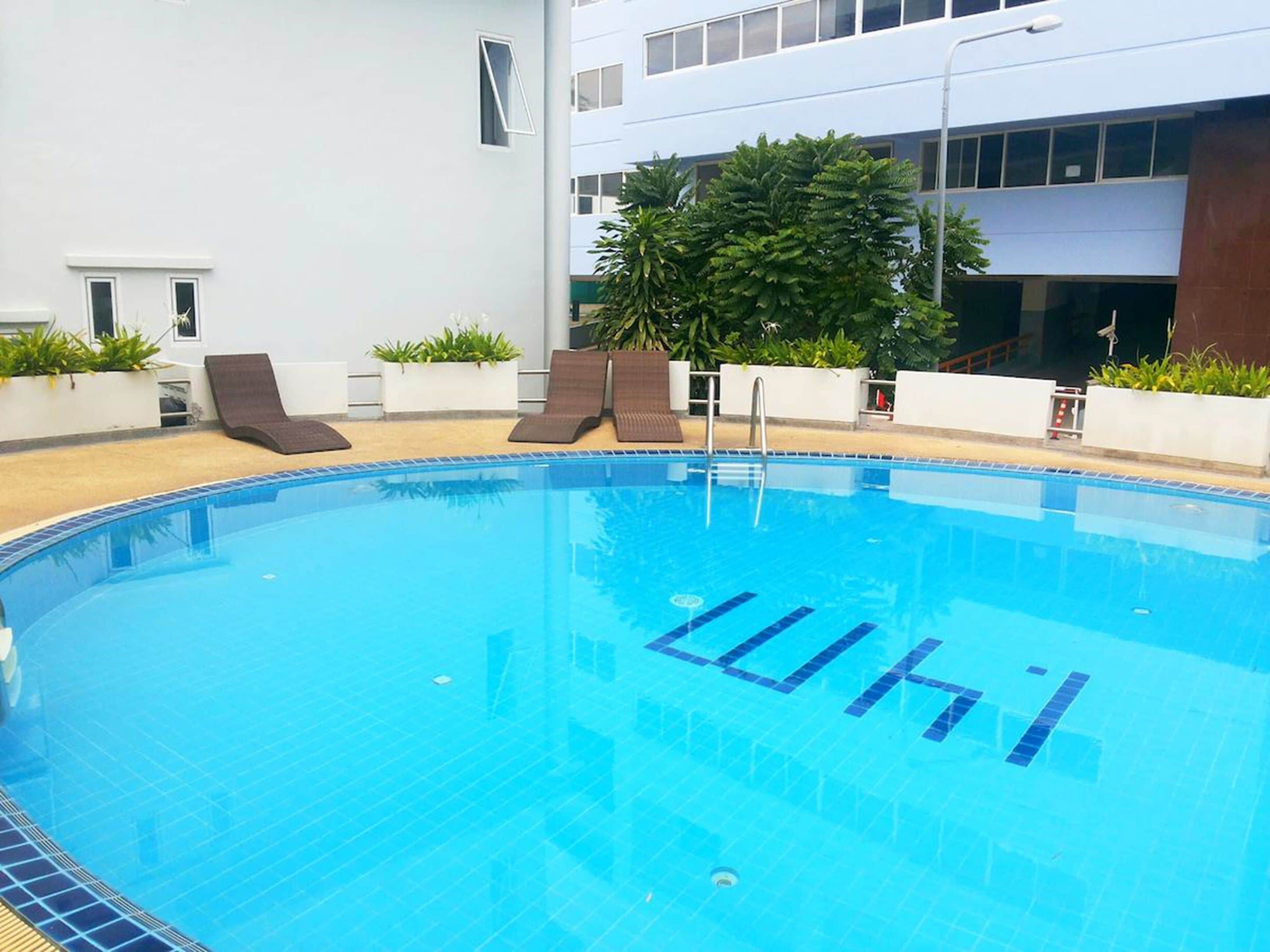 A swimming pool with clear blue water, surrounded by lounge chairs and potted plants.