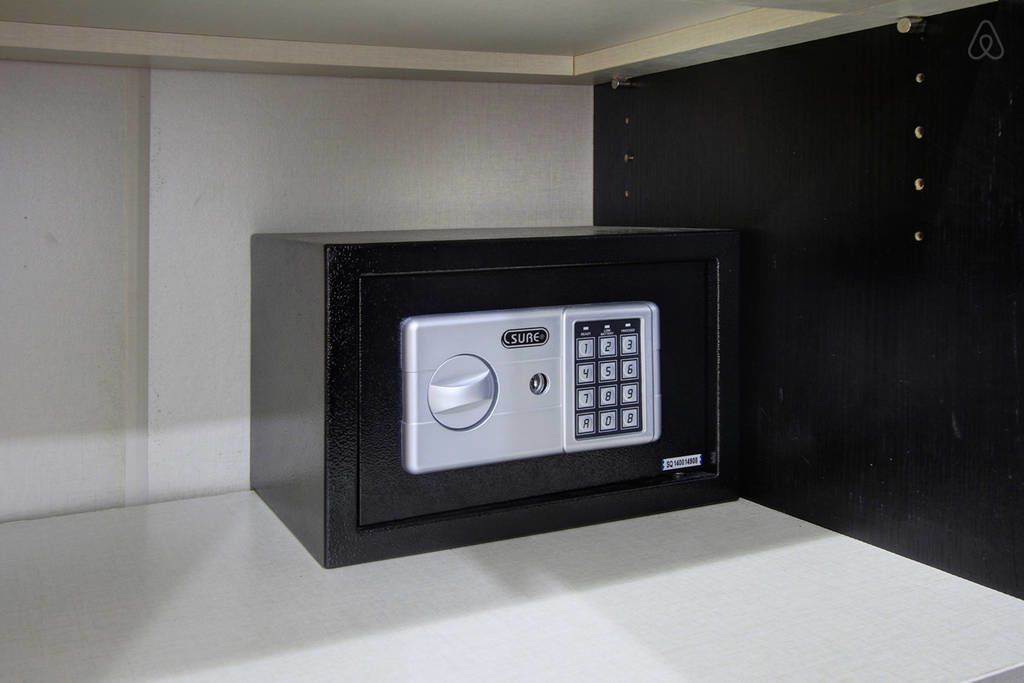 A safe with a keypad and a combination lock, placed on a shelf against a wall.