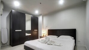 A modern hotel room with a large bed, dark wooden wardrobe, and a mirror.