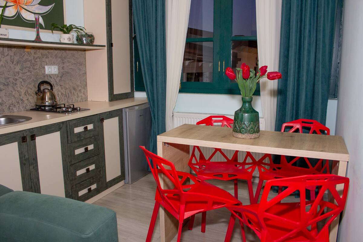 A kitchen with a wooden table, red chairs, a green vase with tulips, and a kettle on the stove.