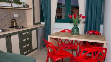 Una cocina con una mesa de madera, sillas rojas, un florero verde con tulipanes y un hervidor en la estufa.