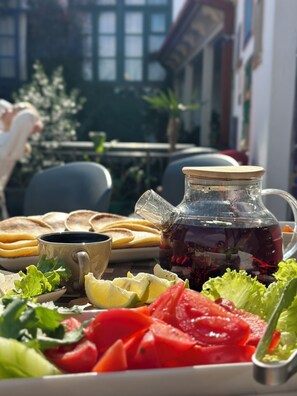 Een tafel met een karaf met donkere vloeistof, mogelijk thee, en een kopje, omringd door diverse etenswaren zoals plakjes tomaat en groen.